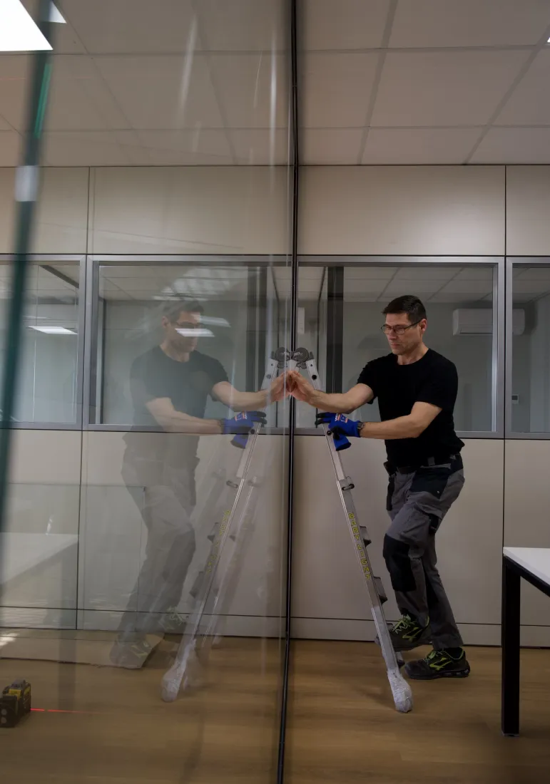 Installatore su una scala che posa una parete in vetro