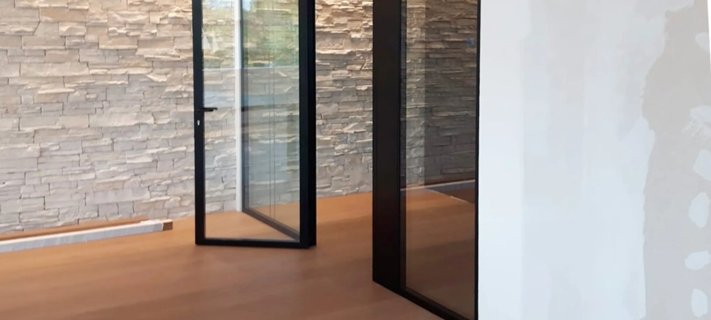Porta in vetro con telaio nero davanti a una parete in pietra